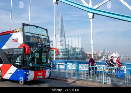 A tourist tour bus travels across Tower Bridge in London alongside a group of people with the Shard skyscraper seen in the background Stock Photo