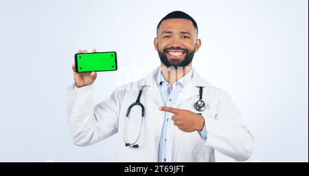Phone, green screen and portrait of doctor pointing to registration, sign up or info in white background. Studio, healthcare and mobile app for Stock Photo