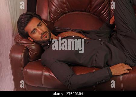 Handsome young man with beard holding roses bouquet sitting at sofa Stock Photo