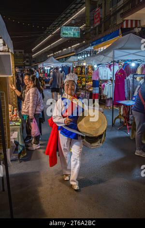 Smiling Thai woman beating a drum as she dances through the Night Market in downtown Chiang Rai, Thailand Stock Photo