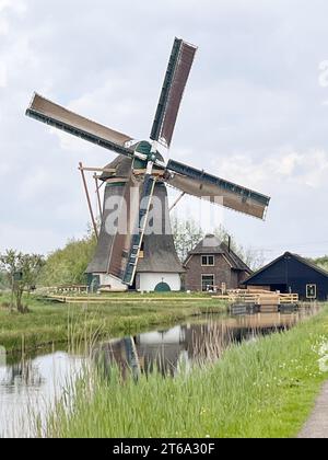 A scenic image of an old windmill standing beside a tranquil body of water, with several small boats sailing on the surface Stock Photo