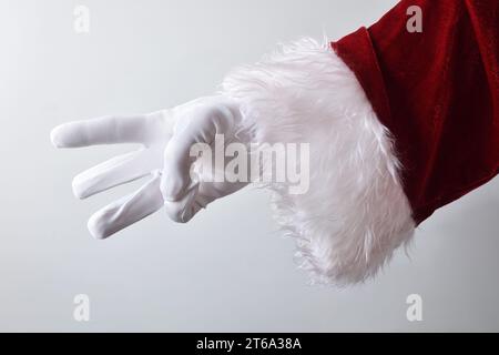 Detail of santa claus hand showing three fingers with white gloves traditionally dressed in red isolated with gradient background behind. Stock Photo
