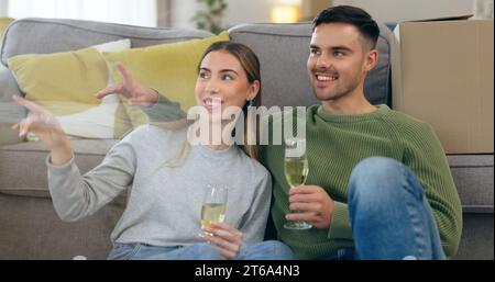 Couple, move and celebration champagne or boxes talking for pointing furniture or living room, chat or happy. Man, woman and new property cheers drink Stock Photo