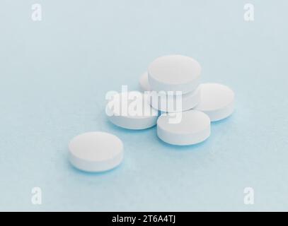 White pills spilled on blue pastel coloured background. Medication and prescription pills. Opioid epidemic. Stock Photo