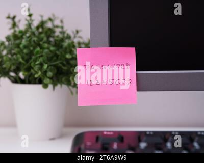 A pink paper note with the reminder Password 12345678 on it sticked on to a monitor at an office workplace. Stock Photo