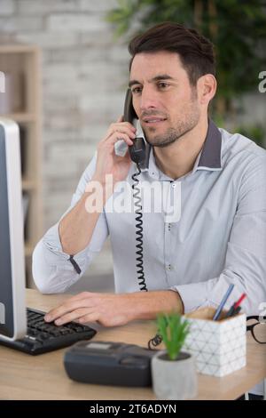 man sat at desk talking on landline telephone Stock Photo
