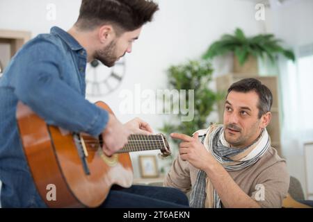 handsome man teaching son to play acoustic guitar at home Stock Photo