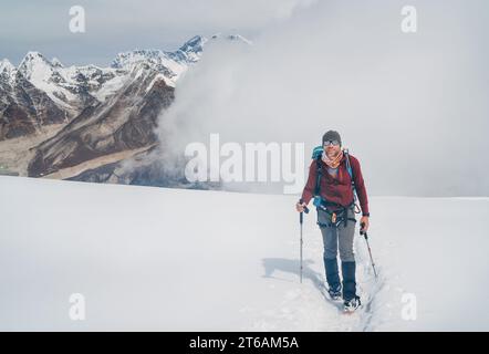 Smiling climber in sunglasses with backpack and trekking poles ascending Mera peak high slopes at 6000m enjoying legendary Mount Everest, Nuptse, Lhot Stock Photo