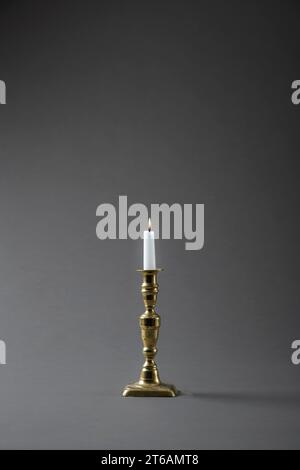 An old brass candlestick with a lit candle, on a plain grey studio background Stock Photo