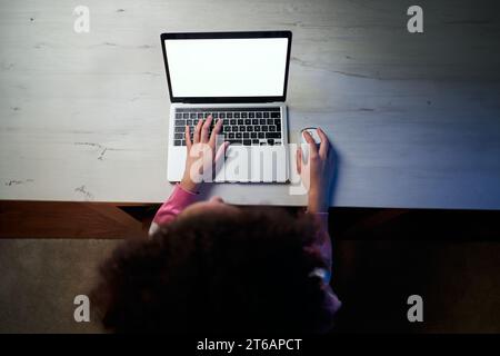 Top view unrecognizable afro woman sitting at table or desk in room using laptop, blank wallpaper.  Stock Photo