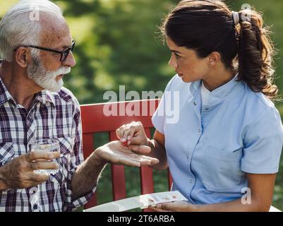 Young nurse giving pills to senior man in park, assisted living and care giving concept Stock Photo