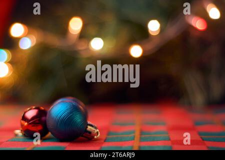 Horizontal Christmas background with Christmas balls on table with green and red tablecloth, blurred Christmas tree and lights. Copy space for text. Stock Photo