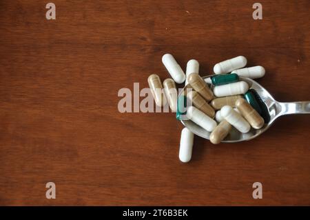 World Antibiotic Awareness Week. Metal spoon with colored pills, antibiotic dietary supplements on brown wooden background.vitamins in a metal spoon Stock Photo