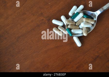 World Antibiotic Awareness Week. Metal spoon with colored pills, antibiotic dietary supplements on brown wooden background.vitamins in a metal spoon Stock Photo