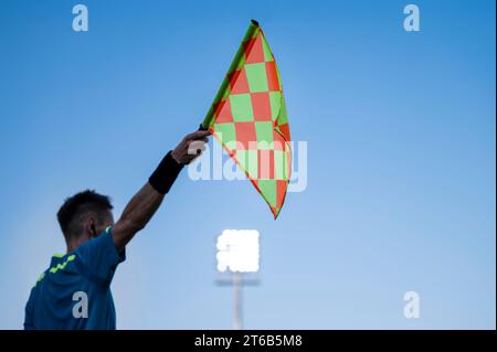 Raised flag of the sideline referee during football match, blue sky and lamps in the background. Stock Photo