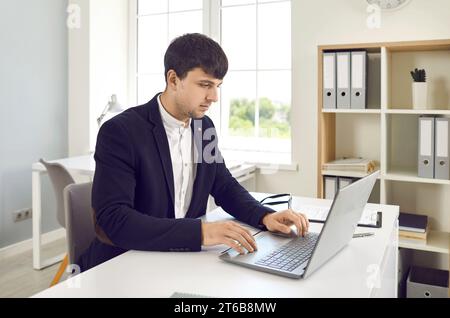 Male office worker works on laptop with electronic documents while sitting in office. Stock Photo