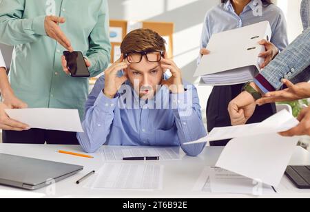 Busy young man gets very stressed and tired of lots of tasks at work in the office Stock Photo