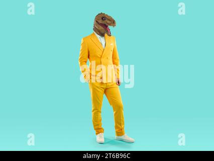 Full-size photo of funny showman in bright yellow suit and white shirt, wearing rubber dinosaur mask on an isolated pale blue background. Stock Photo