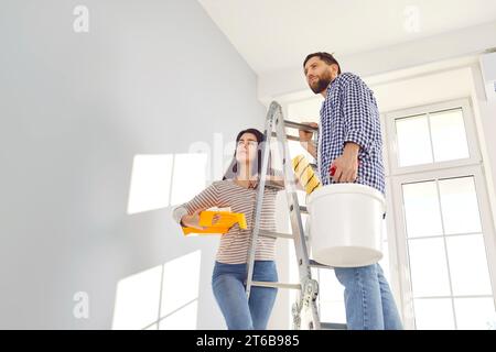 Couple painting their new home holding paint rollers and standing on the ladder. Stock Photo