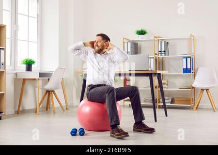 Funny young business man doing sport exercises sitting on fit ball in office. Stock Photo