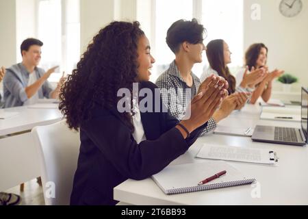 Group of a happy young diverse students applauding to lecturer during a lesson in classroom. Stock Photo