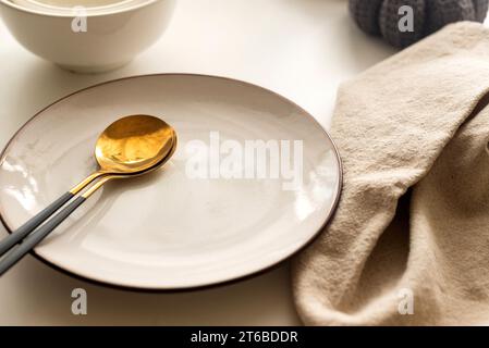 Dinner table setting with white plates and  decorative knite pumpkins on white table top view. Empty modern minimal table setting neutral color Stock Photo