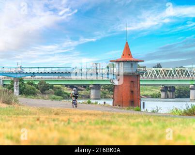 tokyo, japan - jul 18 2023: A man cycling in Japanese countryside along the water intake tower of the Kanamachi water purification plant Stock Photo