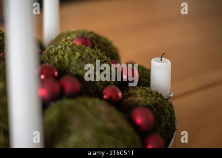 Close-up of a white extinguished candle on an Advent wreath with small red Christmal baubles and moss balls Stock Photo
