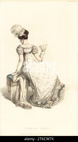 Regency woman in full evening dress seated on a stool, holding a fan, 1820. Evening dress in white figured lace over a satin slip, short puff sleeves, skirt trimmed with satin leaves and flowers, ostrich feathers in the hair. Design by Miss Pierpoint, 9 Henrietta Street, Covent Garden. Plate 35, June 1 1820. Handcoloured copperplate engraving from Rudolph Ackermann's Repository of Arts, London. Stock Photo