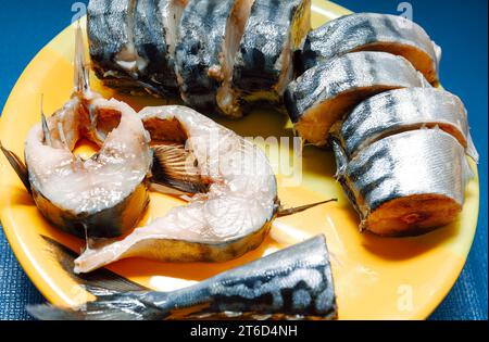 Smoked mackerel on a yellow plate on a blue background . Mackerel slices are arranged neatly on the plate Stock Photo