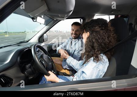 Driving school. Happy student shaking hands with driving instructor during lesson in car at parking lot Stock Photo