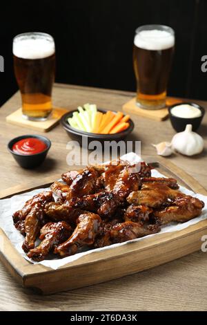Tasty chicken wings, sauces, vegetable sticks and glasses of beer on wooden table. Delicious snacks Stock Photo