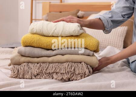 Woman with stack of different folded blankets and clothes on bed in room, closeup. Home textile Stock Photo