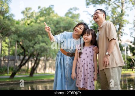Kind and happy Asian grandparents are having fun with their granddaughter, strolling around the public park on a bright day together. Happy family, fa Stock Photo