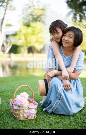 A happy senior Asian grandmother and her cute little girl granddaughter are hugging, enjoying tender moments, and piggy-back cuddling while having fun Stock Photo