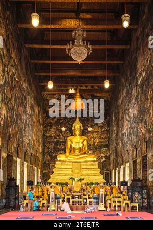 A large sitting, gold Buddha statue dominates the interior altar inside the temple. At Phra Ubosot Wat Suthat in Bangkok, Thailand. Stock Photo
