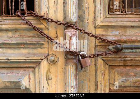 Rusty padlock and chain on an wooden closed entrance door closeup. Abandoned house Stock Photo