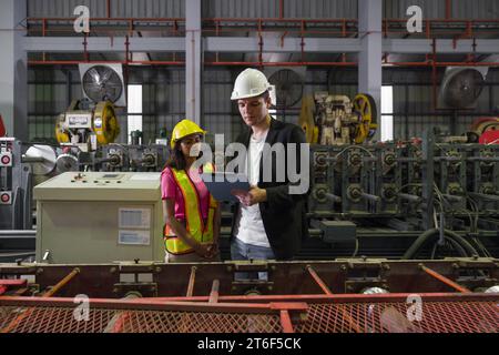 Two workers, wearing hard hats, stand side by side near large machinery at a construction site. Stock Photo