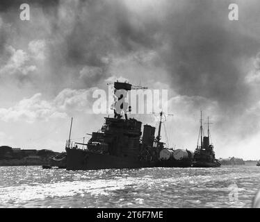 USS Raleigh (CL-7) being kept afloat by a barge lashed alongside, at ...