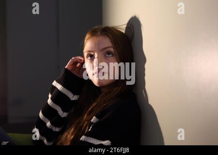 Teenage girl thinking and imagining, hand pushing hair behind her ear, looking upwards Stock Photo