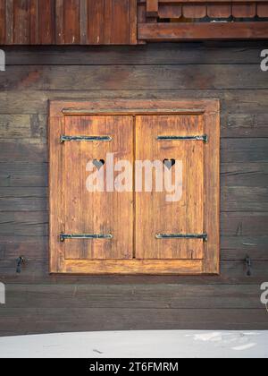 Closed wooden window shutters with heart cut out, rustic vintage design, snow winter, Carinthia, Austria Stock Photo