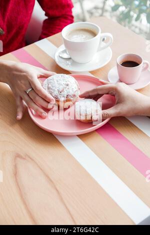 Two Women Holding Pink Jelly Doughnuts Indoors in High Angle View at coffee shop Stock Photo