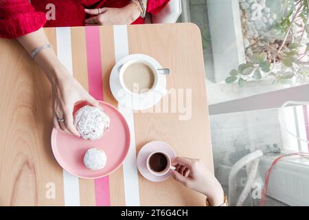 Two Women Holding Pink Jelly Doughnuts Indoors in High Angle View at coffee shop Stock Photo