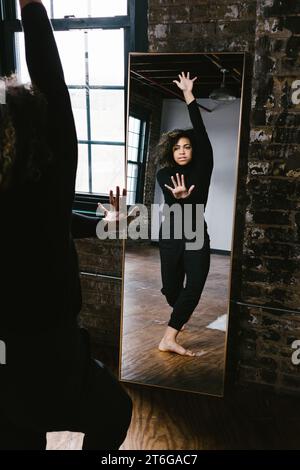 Mixed race female dancer poses with hands stretch in mirror Stock Photo