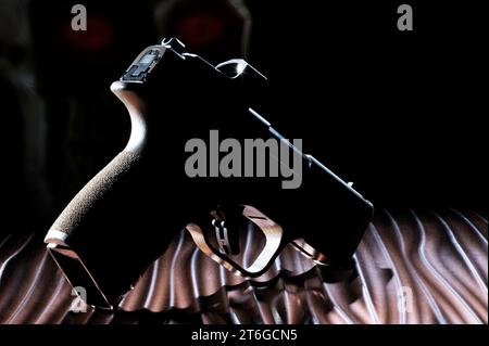 Pistol that is a ghost gun in silhouette with a glowing human skull behind Stock Photo