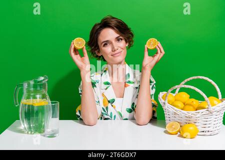 Photo of cute young lady hold two halves ripe lemon showing its vitamins healthcare making juice jug isolated on green color background Stock Photo