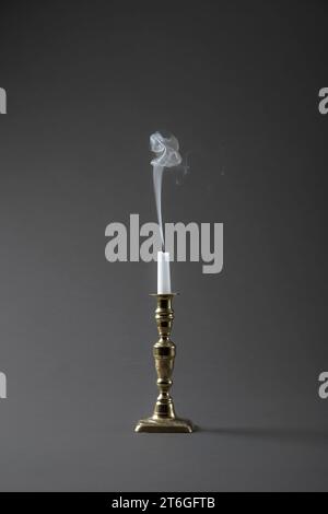 A wisp of smoke rising from a recently extinguished (snuffed) candle in an old brass candlestick, on a plain grey studio background Stock Photo