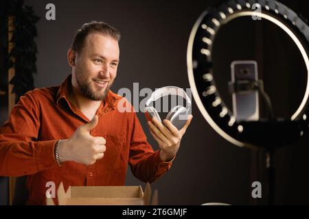 Male techno blogger filming review of new headphones for his channel. Vlogger doing product review on camera, recording headphones recommendation Stock Photo