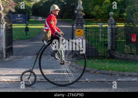 Man riding penny farthing bicycle wearing Victorian British Army tunic and helmet in the London to Brighton veteran car run event, 5th November 2023 Stock Photo