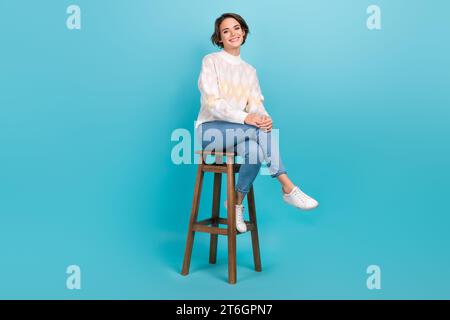 Full body cadre of cheerful attractive girl sitting wooden comfortable chair pub relaxation atmosphere isolated on blue color background Stock Photo
